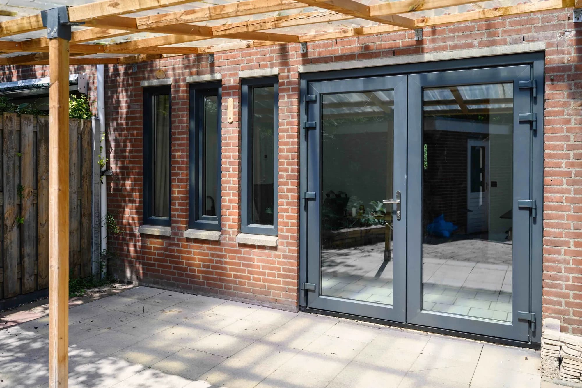 Donkere tuindeuren onder een houten pergola