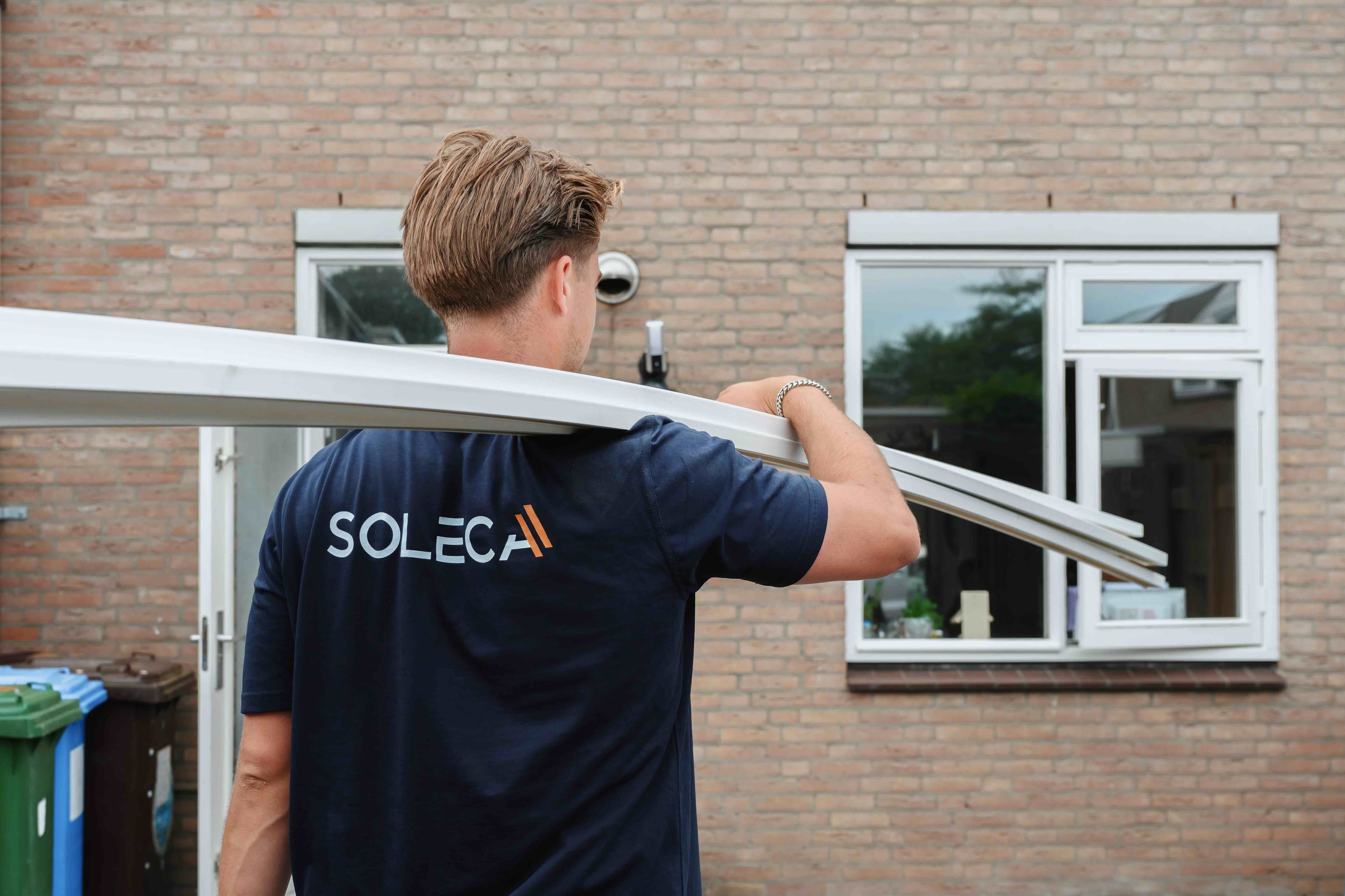 Soleca-monteur draagt een wit kozijn naar een woning