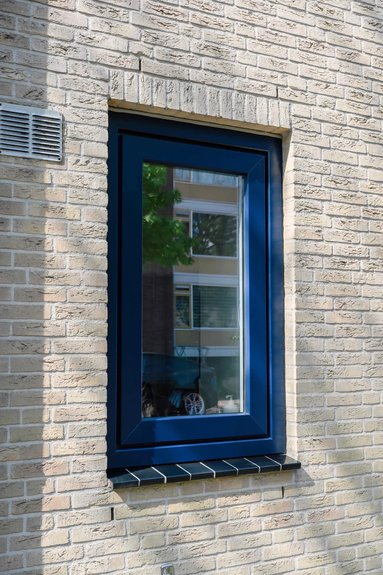 Verticaal donkerblauw raamkozijn in lichte baksteen