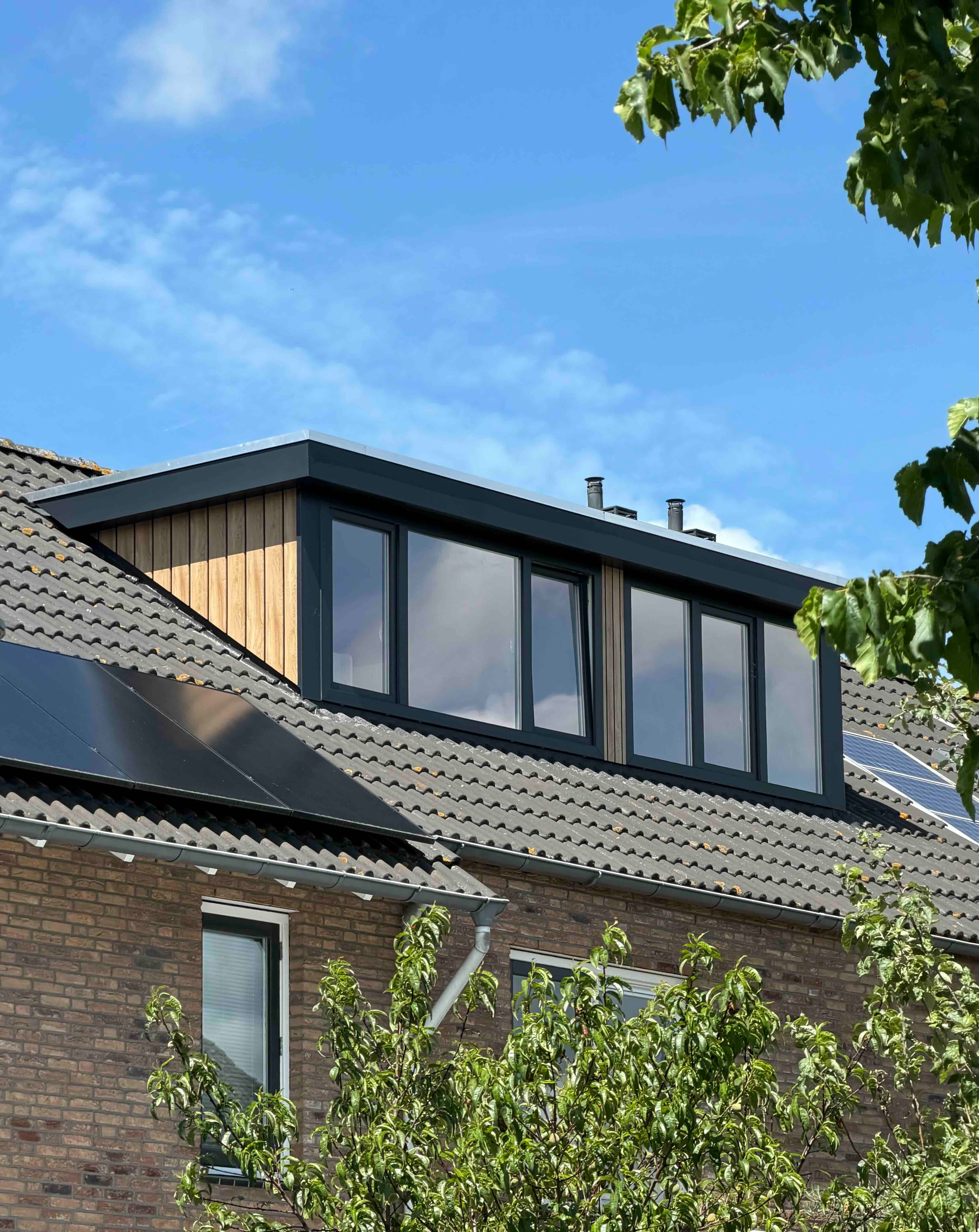 A flat-roof dormer with anthracite frames and a timber cheek on a tiled roof